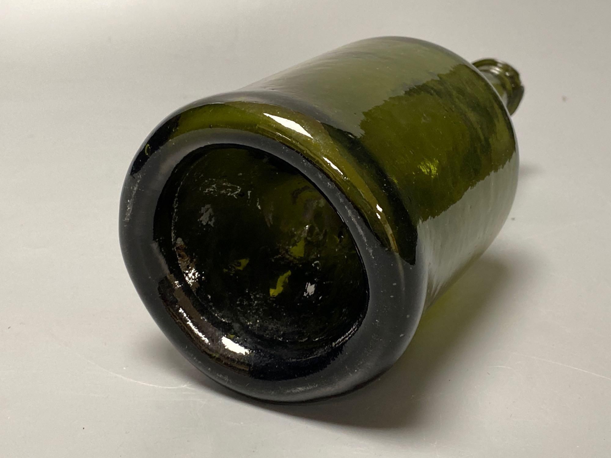 An early 18th century dark green glass wine bottle with a kick in based, 23cm